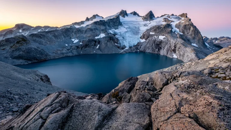 A glacial lake surrounded by rocky peaks at dawn
