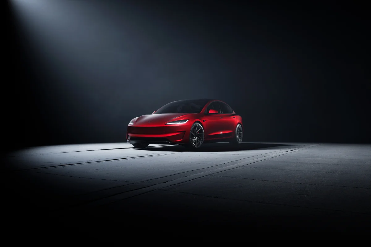 A red Tesla Model 3 in a beam of spotlights
