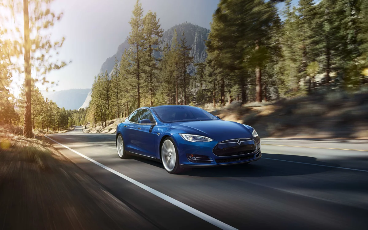 Синій електромобіль Tesla Model S на лісовій дорозі у променях призахідного сонця