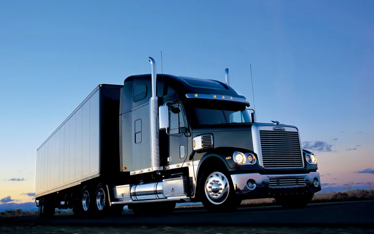 A black Freightliner Coronado tractor-trailer against the backdrop of the pre-sunset sky