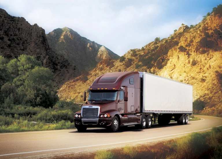 A Freightliner Columbia truck against a backdrop of sun-drenched rocky mountains