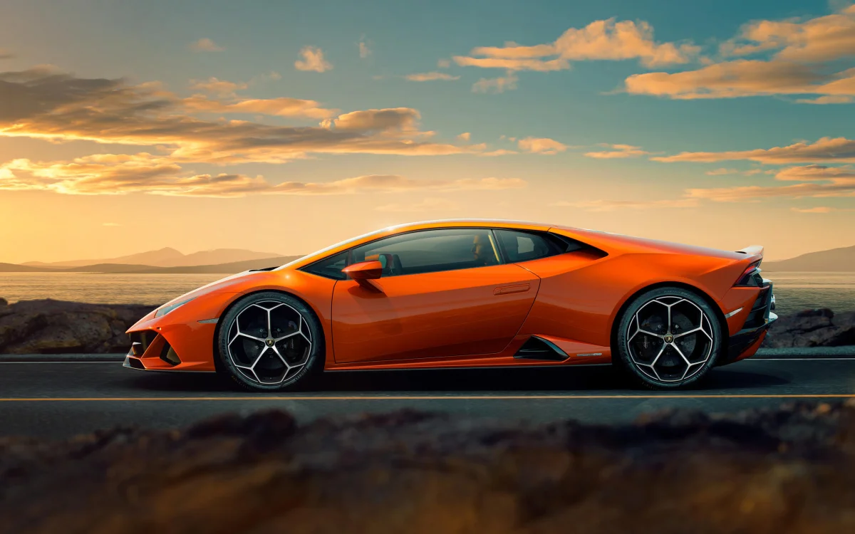 An orange Lamborghini Huracán against the backdrop of a sunset over the sea