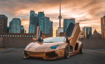 A golden Lamborghini Aventador against the backdrop of Toronto at dusk