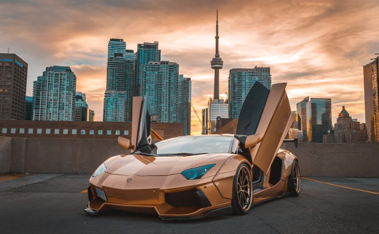 A golden Lamborghini Aventador against the backdrop of Toronto at dusk