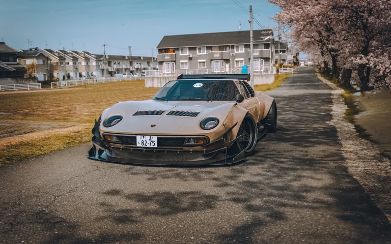 A modified Lamborghini Miura against a backdrop of cherry blossoms in a Japanese suburb