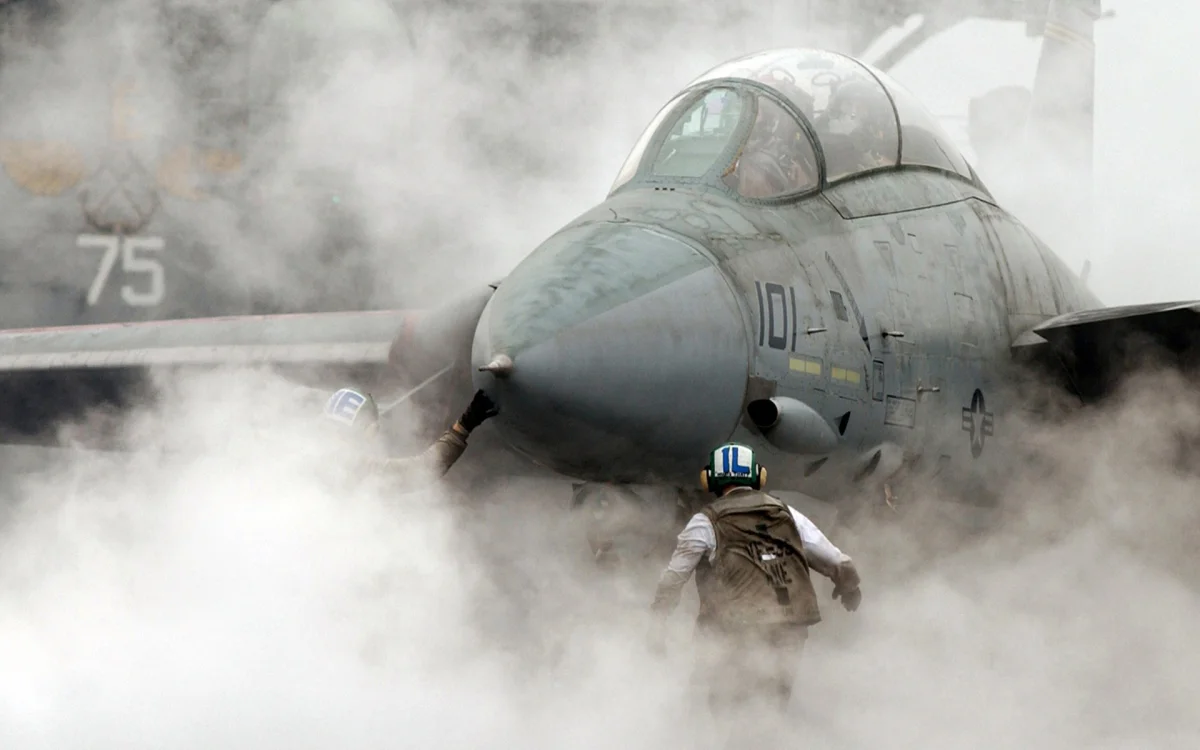 Deck mechanics prepare an F-14 Tomcat fighter jet for takeoff amid a thick cloud of steam