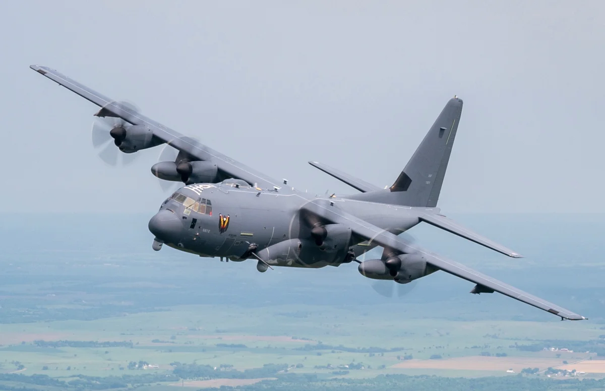 A Lockheed C-130 Hercules military transport aircraft in the sky above the plain