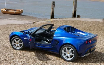 A blue Lotus Elise on a pebbly beach by the water